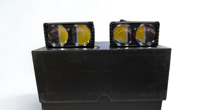 Two black square lights with yellow lenses on a black stand against a white background