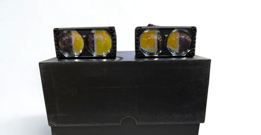 Two black square lights with yellow lenses on a black stand against a white background